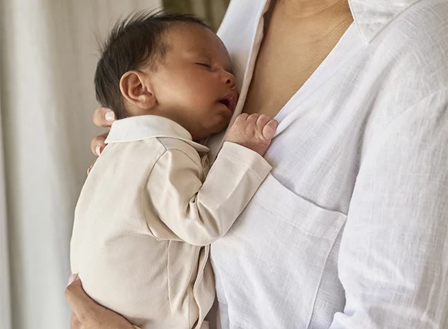 Newborn baby wearing a baby hat and a babygrow.
