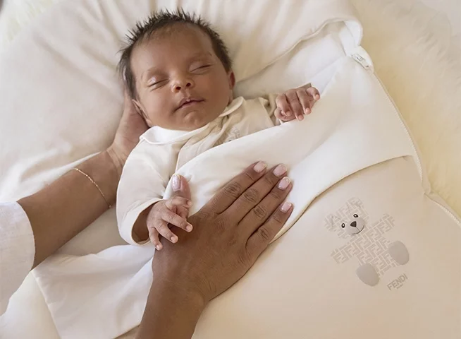 Newborn baby wearing a white baby grow and matching baby hat.