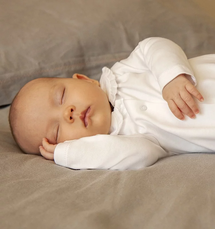 baby kneeling on a large bed, wearing a sleepsuit and hat outfit ready to go to sleep